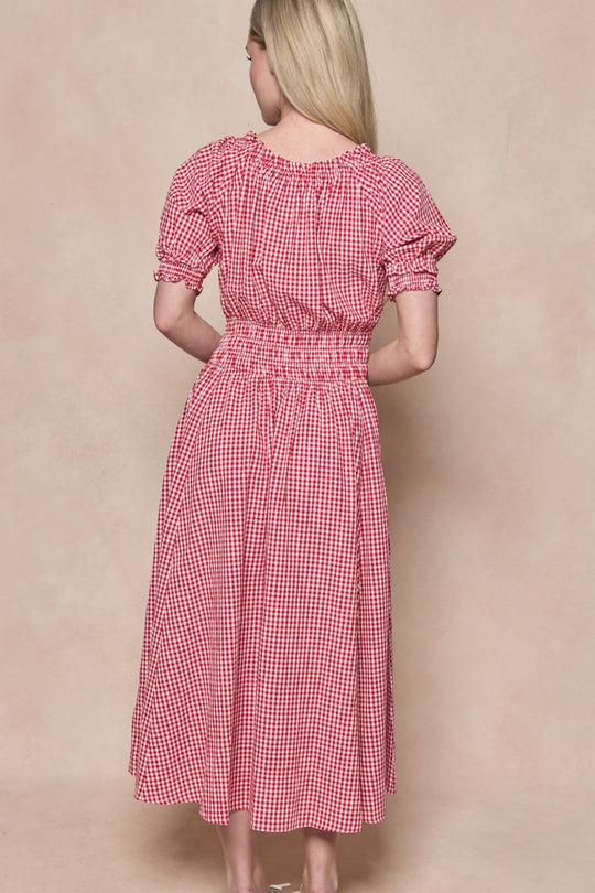 A woman with long blonde hair stands with her back to the camera against a neutral background, wearing the Ivy City Co Jessie Dress in Red Gingham, featuring puff sleeves and a smocked waist.
