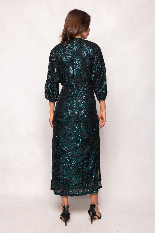 Woman wearing a dark green sequin dress against a white background