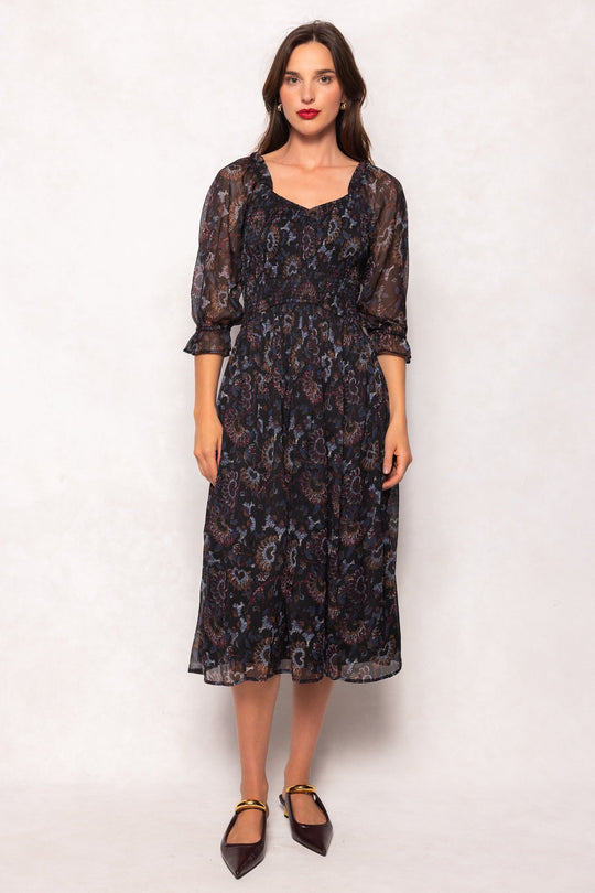 A woman with long brown hair stands against a light background wearing the Maddison Dress in Enchanted Floral by Ivy City Co—a sheer black midi dress adorned with a delicate floral pattern and three-quarter sleeves. She completes her look with dark pointed-toe flats. This style is also maternity friendly.