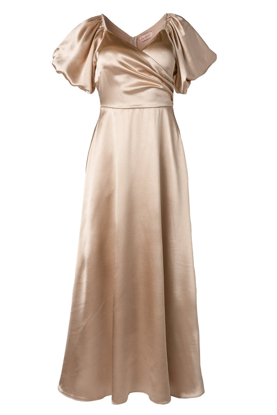 The Tessie Dress in Champagne by Ivy City Co is an elegant, floor-length satin bridesmaid dress featuring short puff sleeves, a v-neckline, and a fitted bodice with a subtle wrap design.