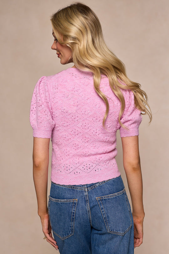 A woman with long blonde hair, wearing the Ivy City Co Michaela Cardigan in Pink and blue jeans, captures women’s spring fashion as she stands with her back to the camera against a beige background.