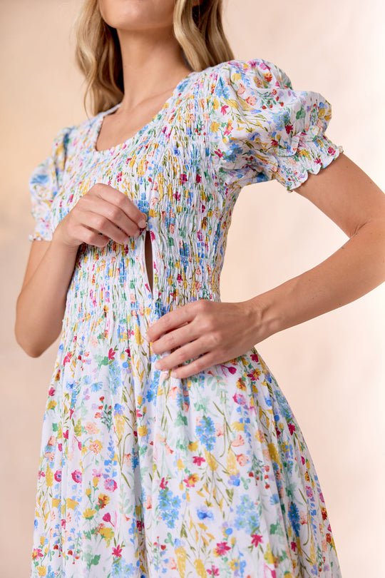 A woman wearing the Amelie Dress in Floral Fields by Ivy City Co showcases a discreet side zipper pocket, holding the fabric open with her right hand. The floral pattern and convenient pocket feature emphasize its appeal as a stylish, nursing-friendly dress.