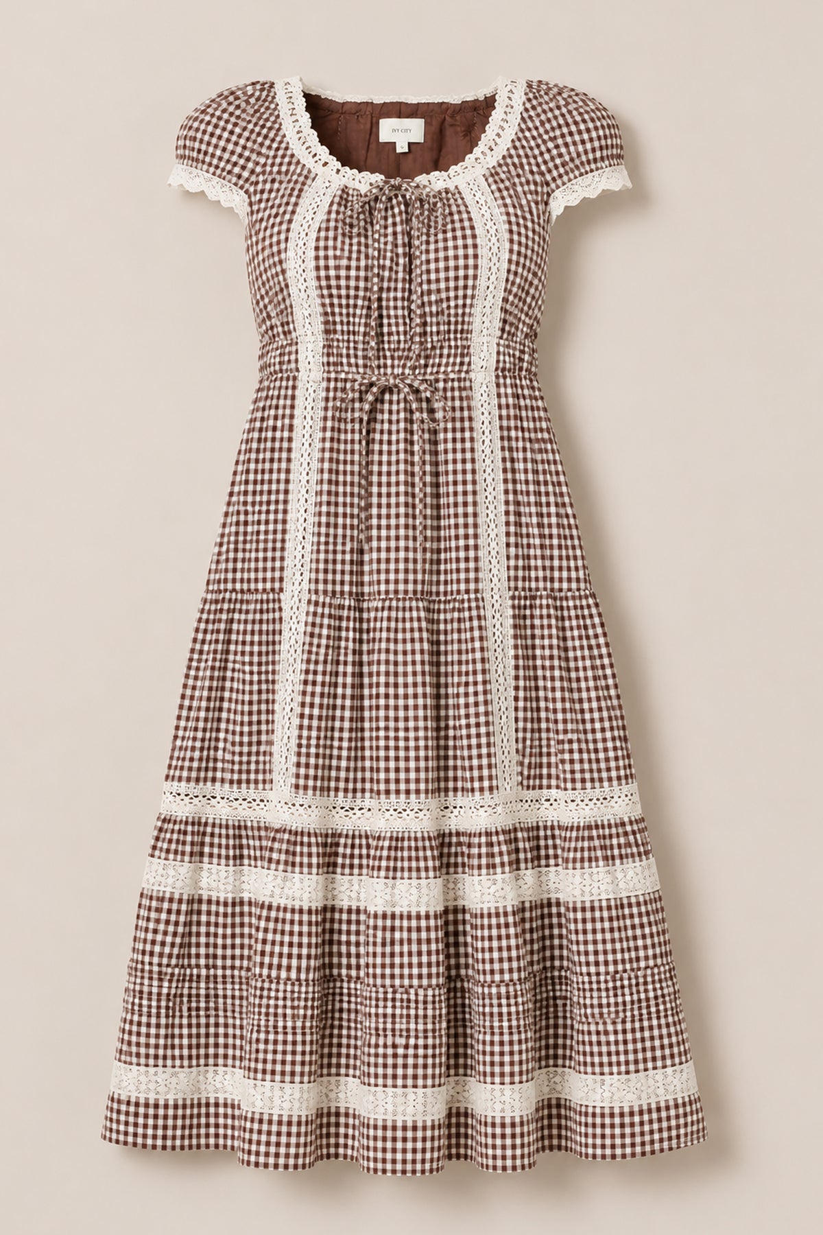 The Palermo Dress in Hickory Gingham by Ivy City Co features a brown and white gingham pattern with short puff sleeves, lace trim, a gathered waist, and a tiered skirt. Displayed on a neutral background, this maternity-friendly dress ensures comfortable style at every stage.