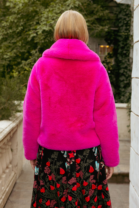 Person wearing a bright pink fur coat with a blurred background