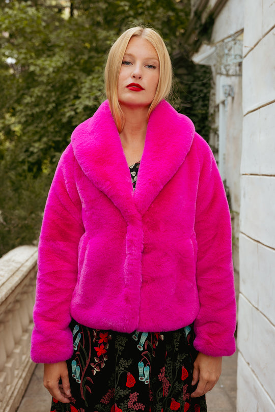 Woman wearing a bright pink fur coat standing outdoors.