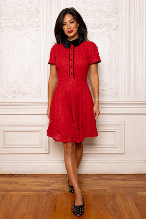Woman wearing a red dress with a black collar against a white wall.