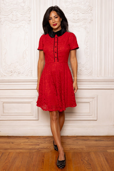 Woman wearing a red dress with a black collar against a white wall.