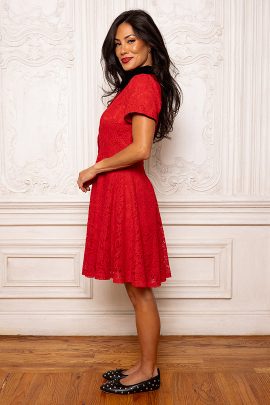 Woman wearing a red dress standing against a white wall.