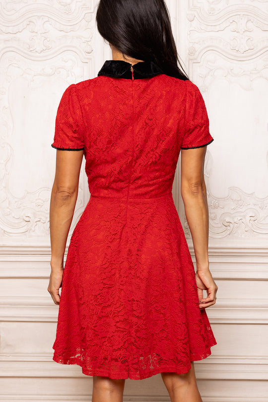 Red lace dress with black trim worn by a person against a white wall.