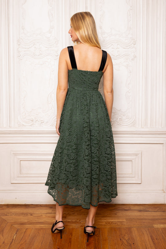 Woman wearing a green lace dress standing against a white wall.