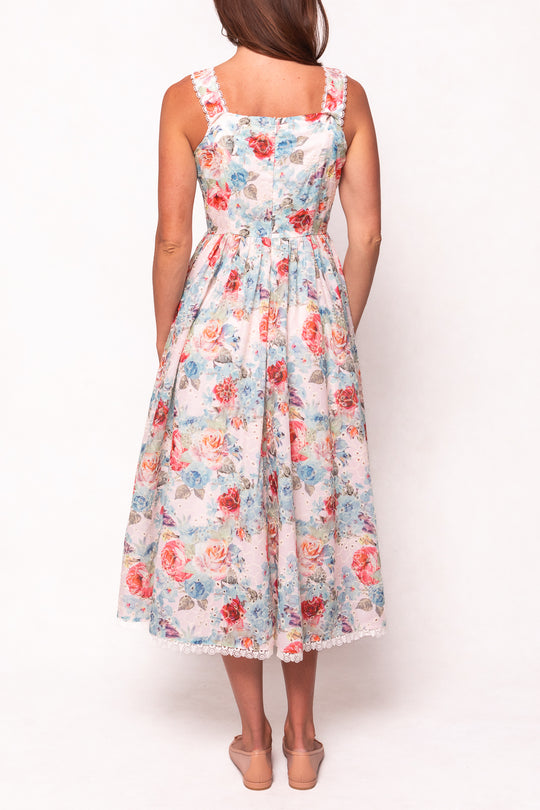 A woman seen from the back wears the Ivy City Co Penny Tank Midi Dress in Multicolor Floral—a sleeveless, ankle-length cotton eyelet dress with a fitted waist and full skirt in pink, red, and blue flowers. She pairs it with nude low-heeled shoes.