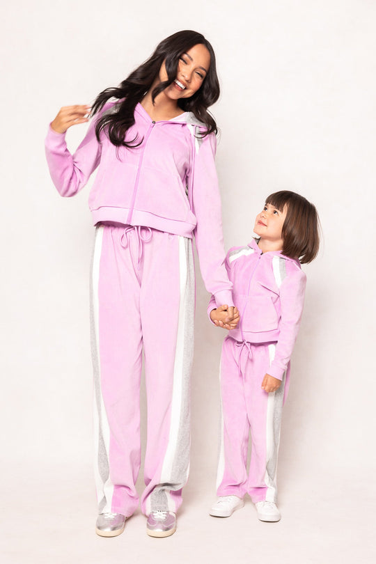 A woman and a young girl, both dressed in the Ivy City Co Mini Kailey Zip Up Velour Sweatshirt in Pink, stand holding hands and smiling against a light background.