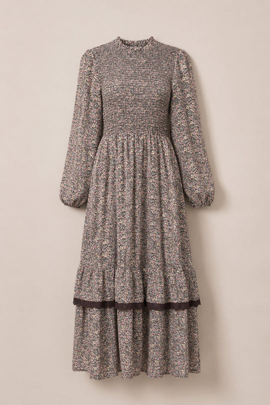 The Presley Dress in Ditsy Autumn Fleur by Ivy City Co is a long-sleeved, ankle-length maxi dress with a high neckline, smocked bodice, and tiered skirt. This charming fall dress features a small, multicolored floral pattern on a muted background.