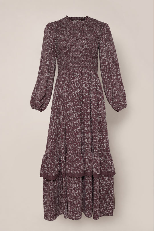 The Presley Dress in Mahogany Ditsy by Ivy City Co is a long-sleeved, burgundy midi dress adorned with a delicate white ditsy print, featuring an elegant smocked bodice, ruffled tiered skirt, and graceful balloon sleeves, shown against a simple light background.