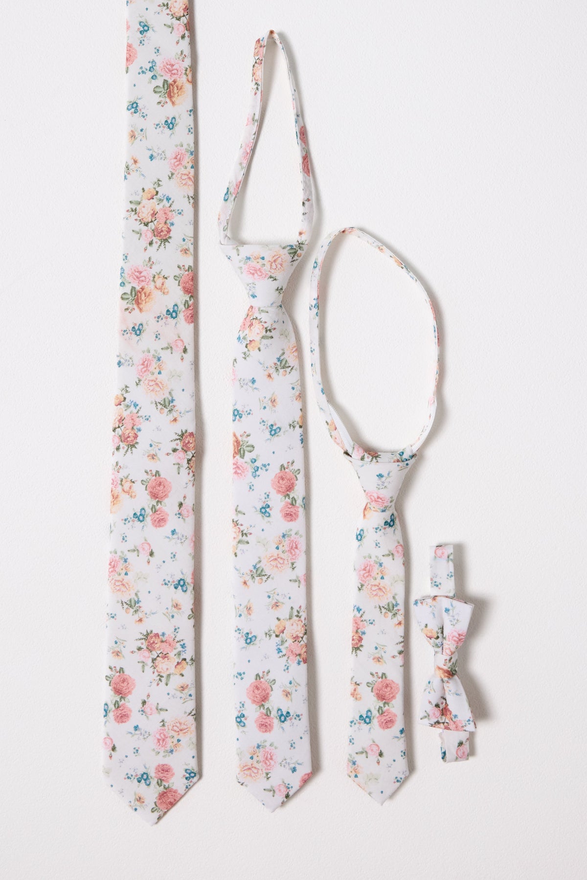 Four white ties and bow ties by Ivy City Co, adorned with the charming Countryside Peony Blossom design, are arranged vertically against a white background. These coordinated accessories are available in styles for adults, children, and infants—perfect for creating a matching family look.