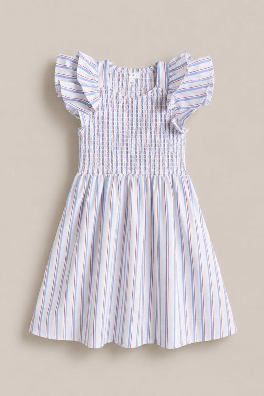 Introducing the Mini Hattie Dress in Heritage Stripe by Ivy City Co—a delightful children’s dress featuring flutter sleeves, a smocked bodice, and a flared skirt. Crafted from white fabric adorned with vertical red and blue stripes, it’s an ideal choice for Fourth of July celebrations. The dress is shown against a neutral background.
