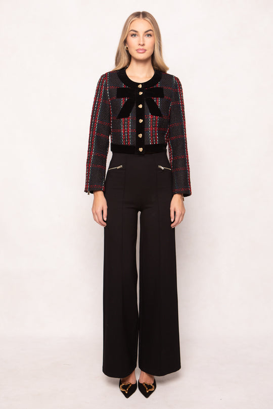 Woman wearing a patterned jacket with a bow and black pants on a white background