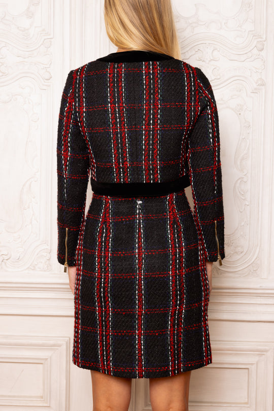 Person wearing a black and red plaid dress against a white wall.