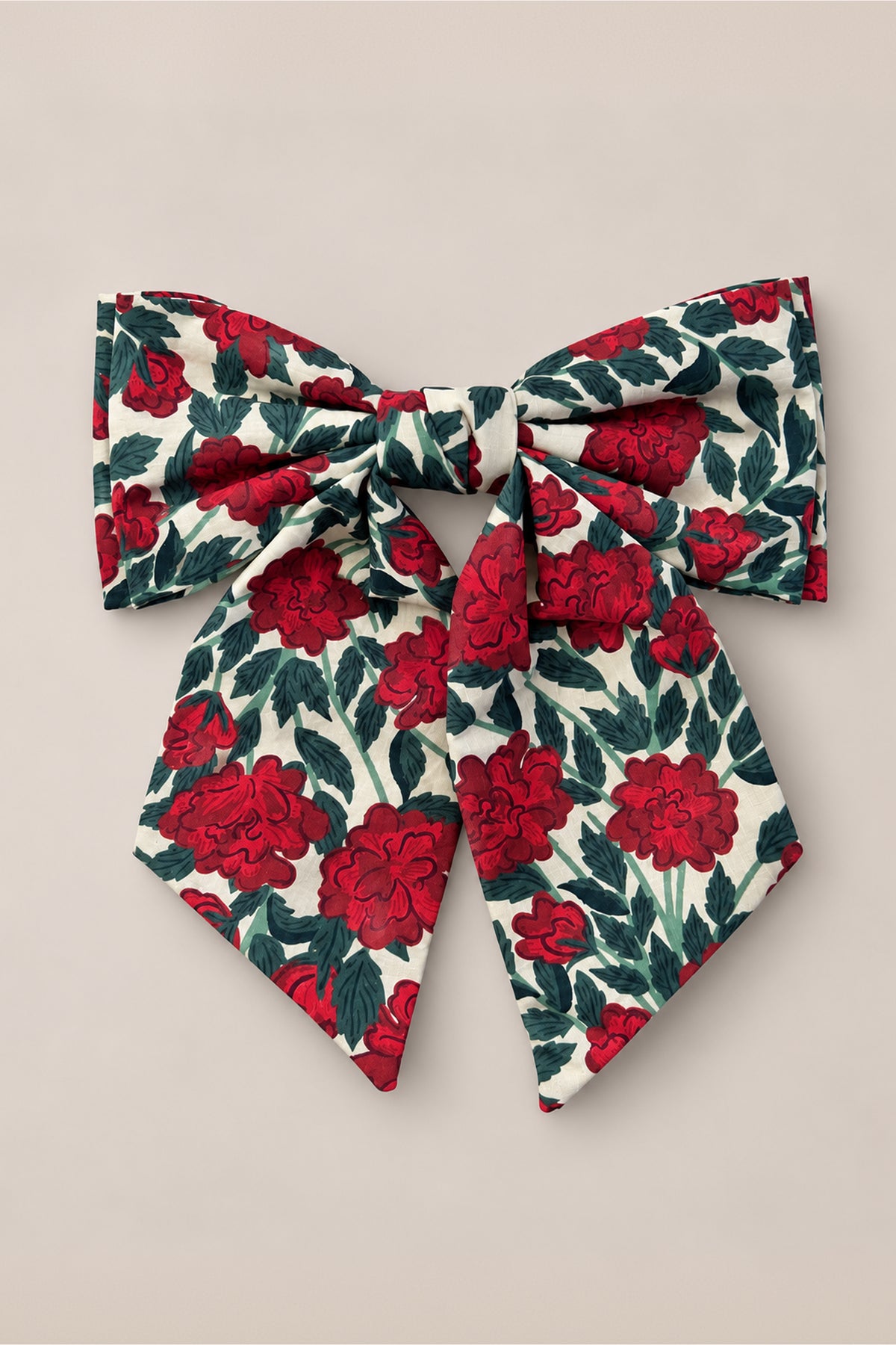 The Hair Bows in Red Roses from Ivy City Co feature a rose floral print with vibrant red flowers and green leaves on a crisp white background, styled against a neutral beige surface for a timeless vintage Christmas charm.