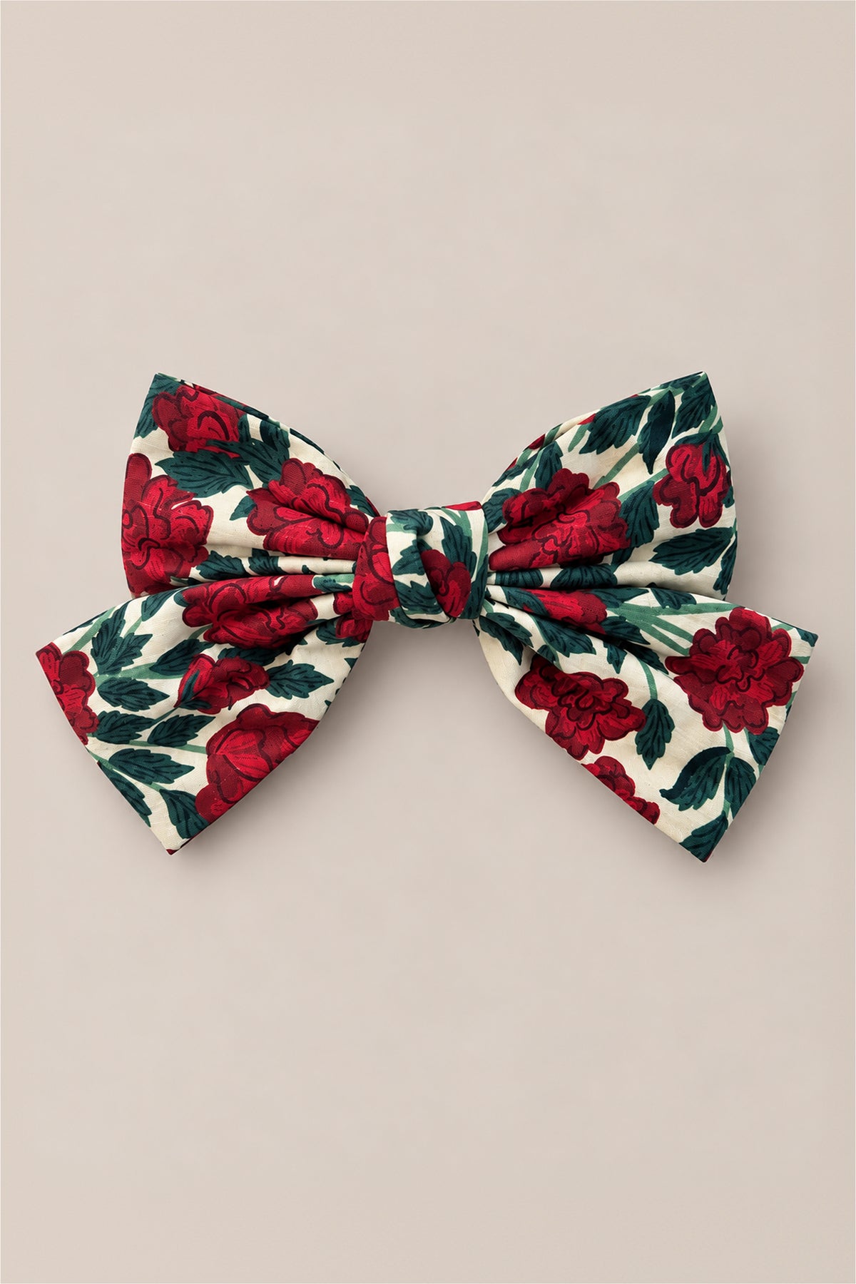 The Ivy City Co Hair Bows in Red Roses feature a large fabric bow with a rose floral print of red roses and green leaves on a cream background, offering a charming vintage Christmas vibe. Displayed against a plain beige surface.