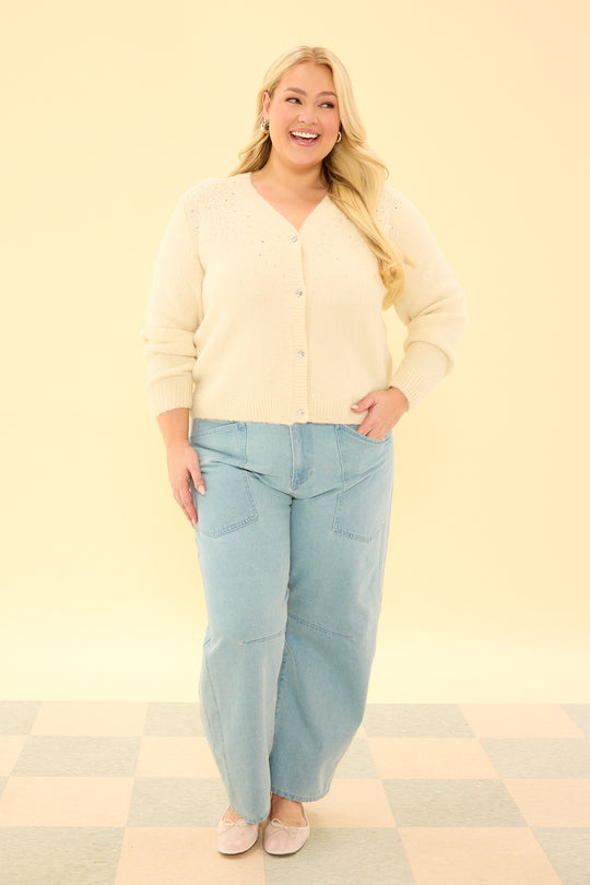 Woman wearing a light yellow cardigan and light blue jeans on a yellow background