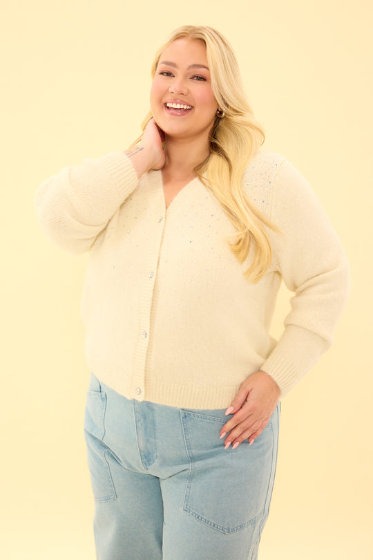 Woman wearing a light yellow cardigan and light blue jeans against a yellow background