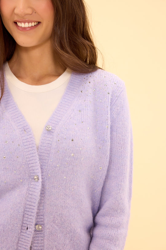 Person wearing a light purple cardigan with a beige background