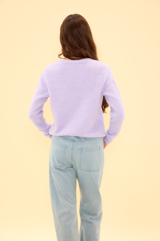 Person wearing a light purple sweater and light blue jeans on a yellow background