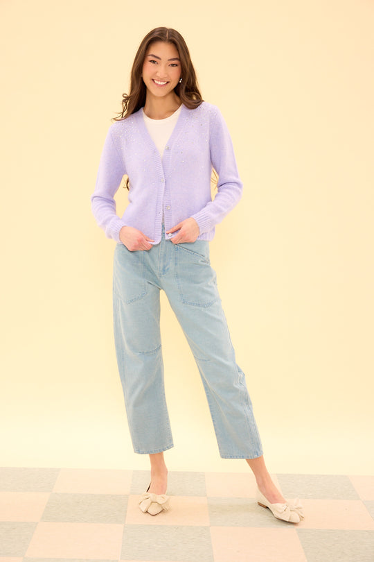 Woman wearing a light purple cardigan and light blue jeans on a beige background