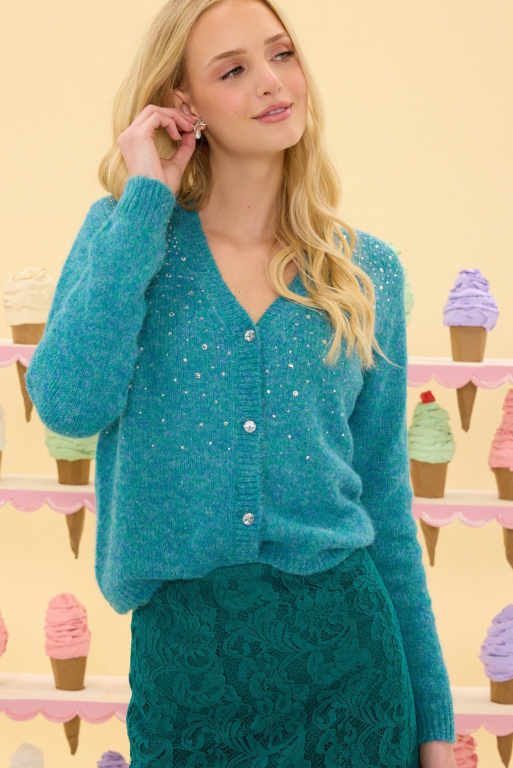 Woman wearing a teal cardigan over a green lace dress with an ice cream cone patterned background.