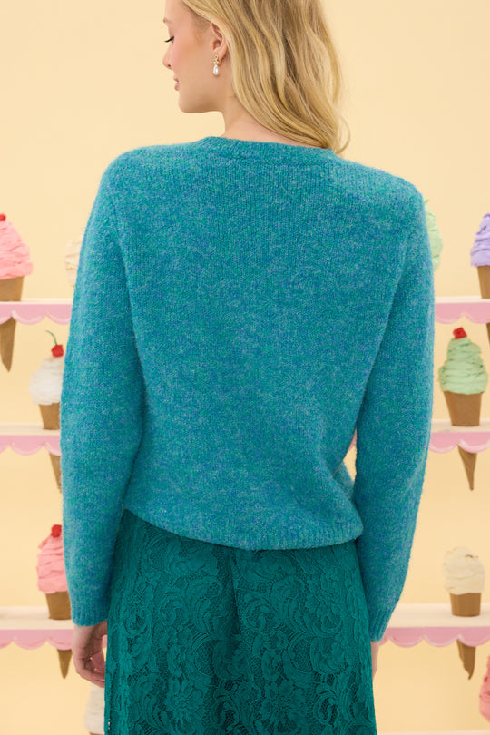 Woman wearing a teal knitted cardigan with a pastel ice cream cone display in the background