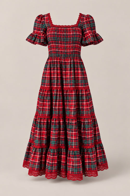 The Rosario Dress in Christmas Cheer Plaid by Ivy City Co features red plaid fabric, short sleeves, ruffled hems, a smocked bodice, and a long tiered silhouette. Displayed on a neutral background, it’s the perfect maternity-friendly choice or family photo outfit.