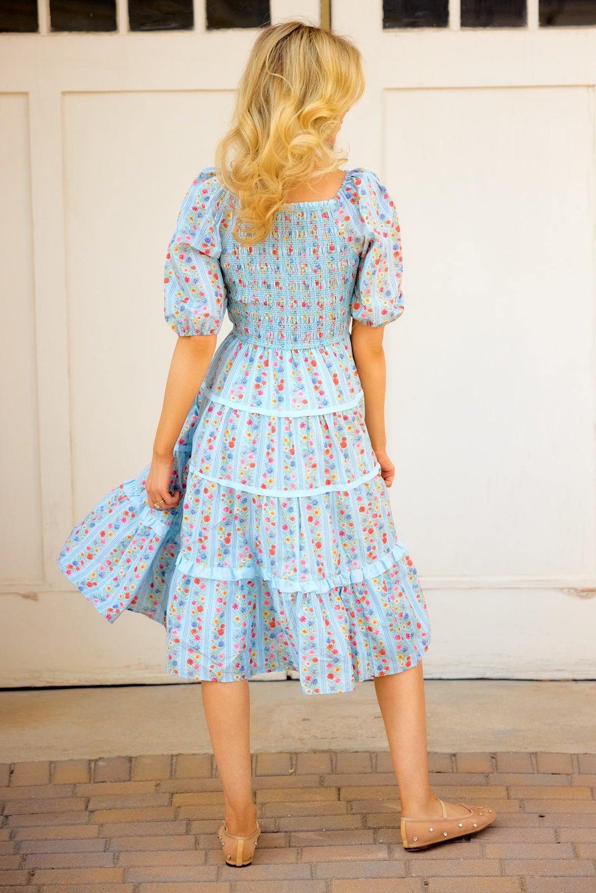 a photo of the back of a woman in a blue floral dress standing outside in front of white barn doors