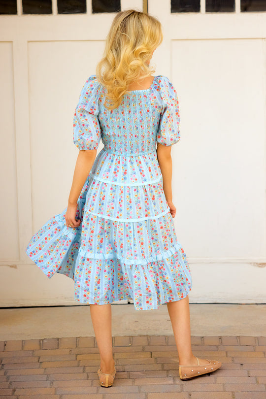a photo of the back of a woman in a blue floral dress standing outside in front of white barn doors