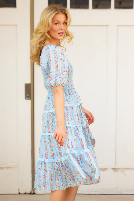 A photo of a woman in motion twirling in a blue dress in front of white barn doors