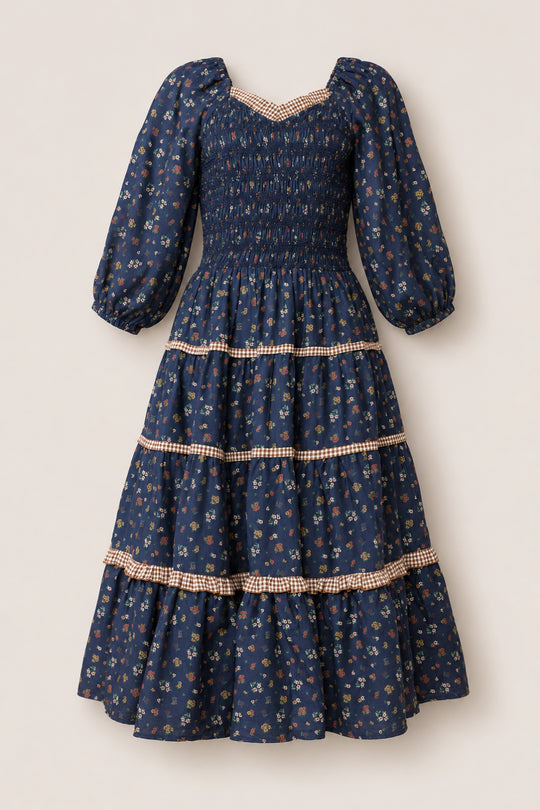 The Roselyn Dress in Midnight Lovelorn Ditsy by Ivy City Co is a navy blue cotton midi dress featuring long puffed sleeves, a smocked bodice, and a charming small floral print. The tiered skirt, finished with tan gingham trim, adds an elegant touch to this maternity-friendly style.