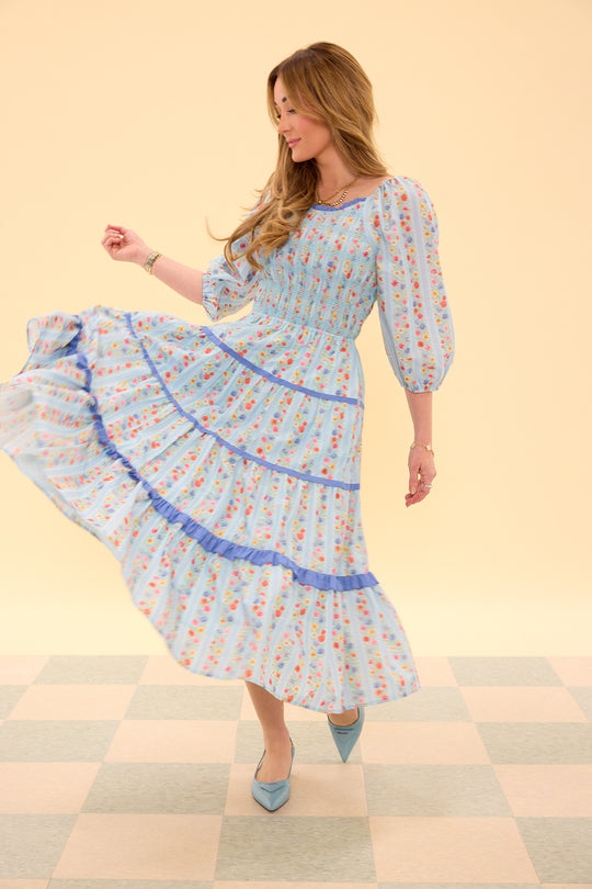 Woman wearing a light blue floral dress on a checkered floor with a beige background