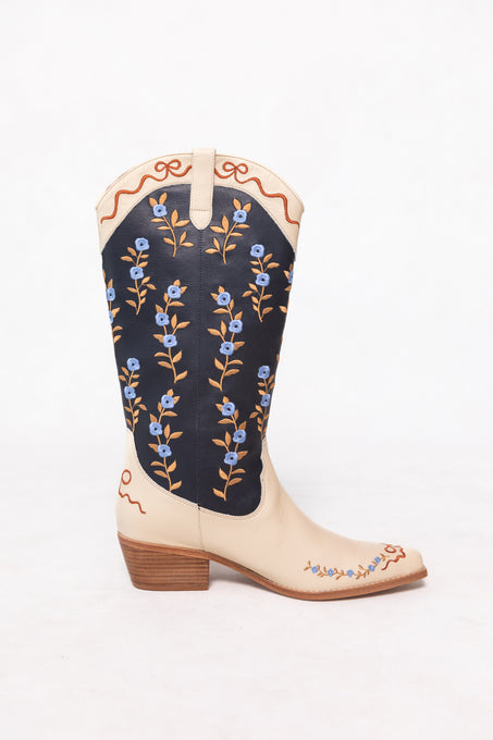 The Rosemary Cowgirl Boots in Cream & Navy by Ivy City Co feature cream leather with navy accents, a low wooden heel, and are adorned with floral embroidery and brown vine details on the shaft and toe.