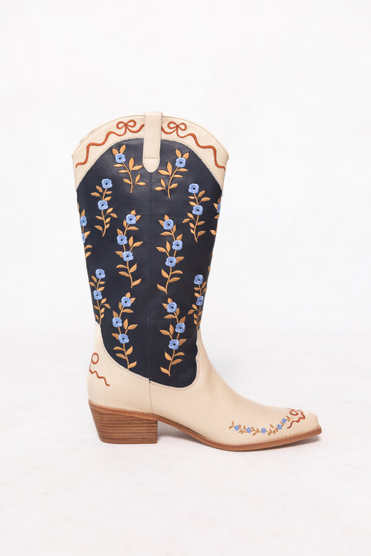 The Rosemary Cowgirl Boots in Cream & Navy by Ivy City Co feature cream leather with navy accents, a low wooden heel, and are adorned with floral embroidery and brown vine details on the shaft and toe.