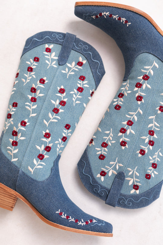 The Rosemary Cowgirl Boots in Denim by Ivy City Co feature light blue panels, red and white floral embroidery, and light brown wooden heels, displayed on a light background.