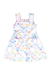 The Ivy City Co Mini Rue Play Dress in Blue Bouquet is a sleeveless girls’ dress with a colorful floral print, pink-trimmed straps, and two heart-shaped skirt pockets, designed in the brand’s playful signature style.