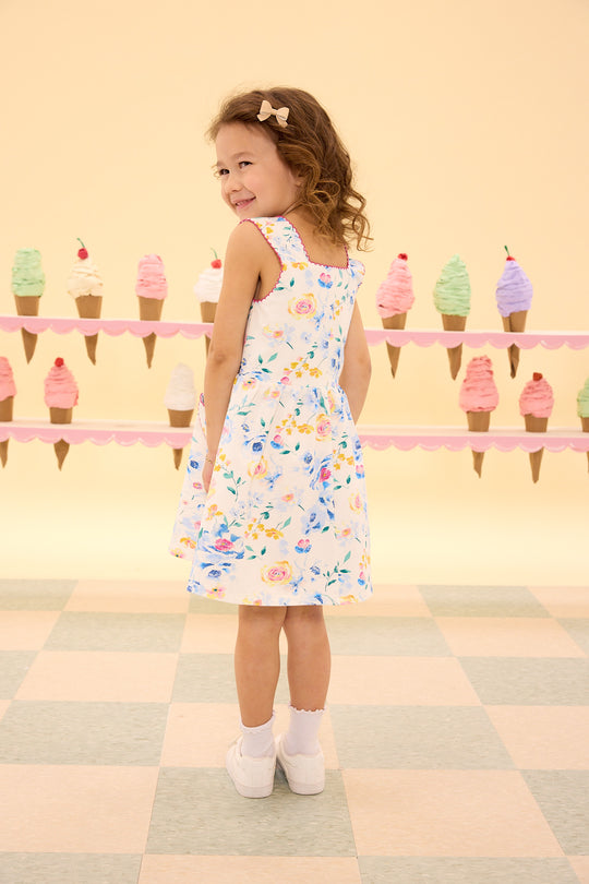 Young girl in a floral dress standing in front of an ice cream cone display.