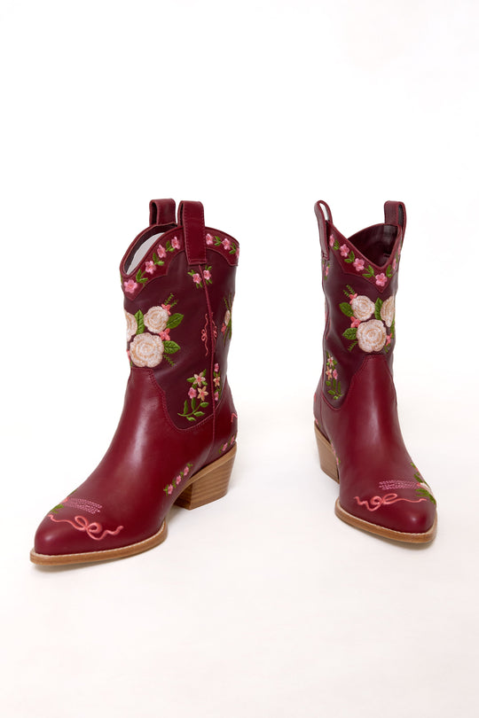 Pair of red cowboy boots with floral embroidery on a white background