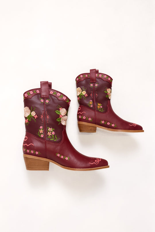Pair of burgundy cowboy boots with floral embroidery on a white background