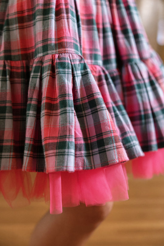 A close-up of the Ivy City Co Scottie Dress in Vibrant Plaid, featuring a cotton blend in pink and green plaid with pink tulle lining underneath and pleated detailing.