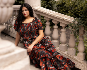 Woman in a floral dress sitting on a stone staircase with greenery in the background
