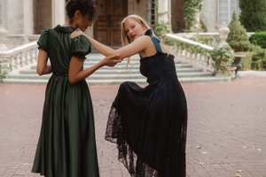 Two women in green and black dresses standing in front of a large house.