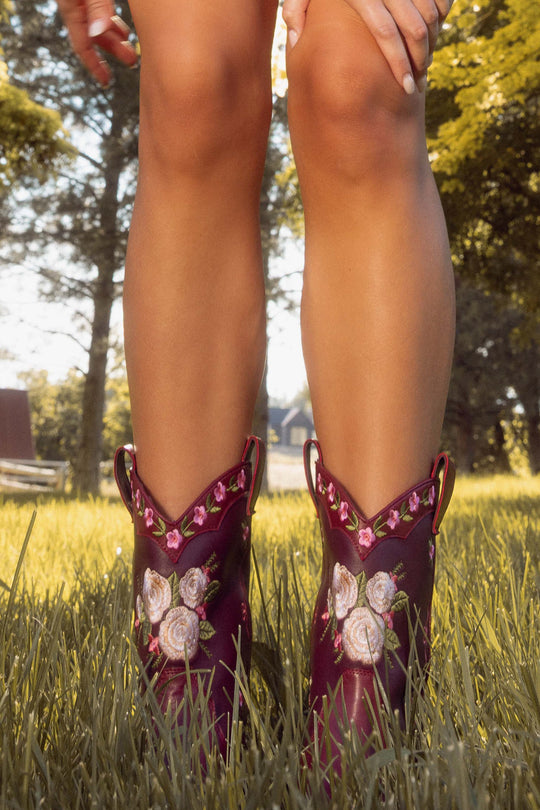 Person wearing burgundy embroidered cowboy boots in a grassy outdoor setting
