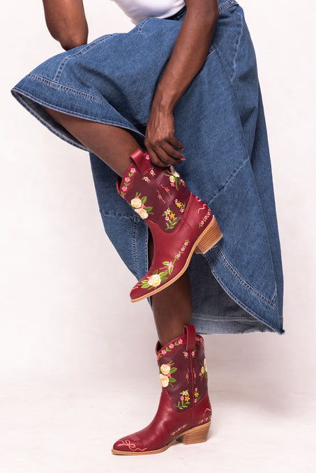 Red embroidered boots worn with a denim skirt on a white background