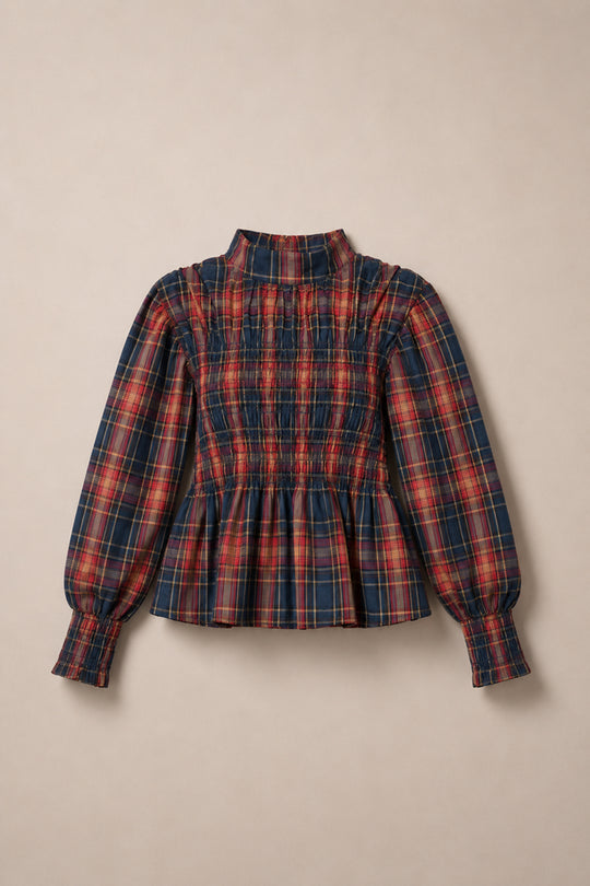 The Sigrid Top in Twilight Plaid by Ivy City Co features a navy and red plaid pattern with a smocked front, mock neckline, balloon sleeves, and a peplum hem, displayed flat on a beige background.